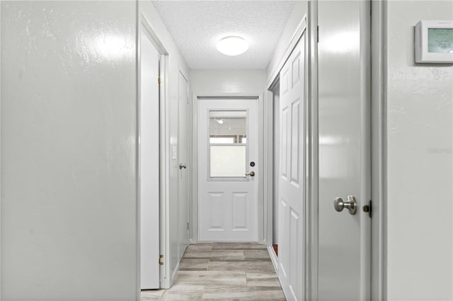 corridor featuring light wood-type flooring and a textured ceiling