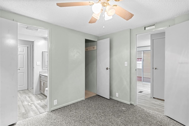 unfurnished bedroom with ceiling fan, ensuite bathroom, light wood-type flooring, and a textured ceiling