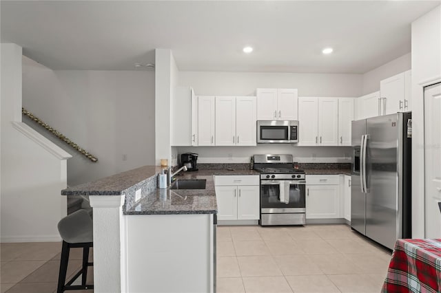 kitchen featuring kitchen peninsula, dark stone counters, a breakfast bar, stainless steel appliances, and white cabinetry