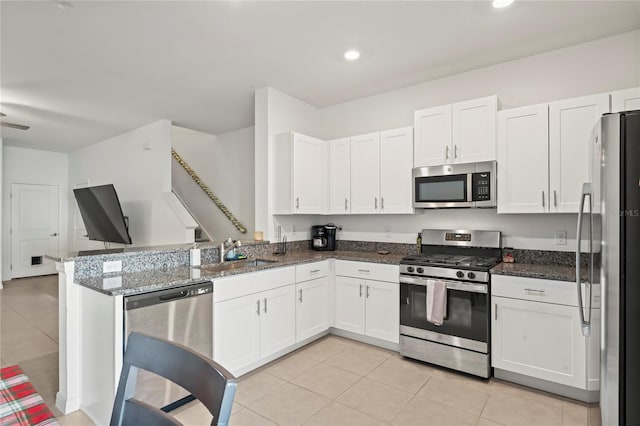 kitchen with kitchen peninsula, white cabinets, dark stone counters, and appliances with stainless steel finishes