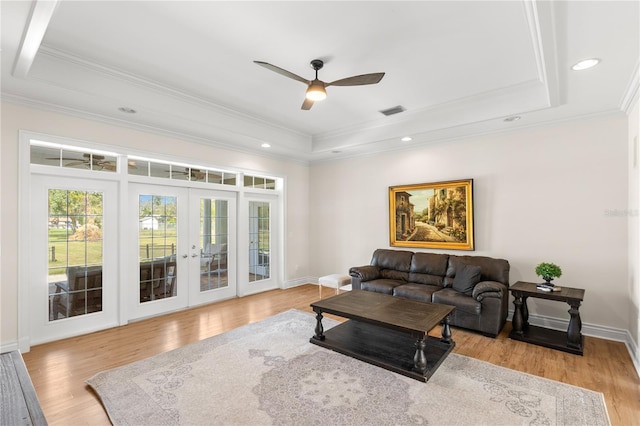 living room with ceiling fan, french doors, light wood-type flooring, a tray ceiling, and ornamental molding