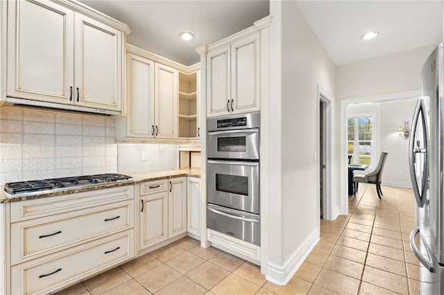 kitchen with cream cabinets, decorative backsplash, light tile patterned floors, appliances with stainless steel finishes, and light stone counters