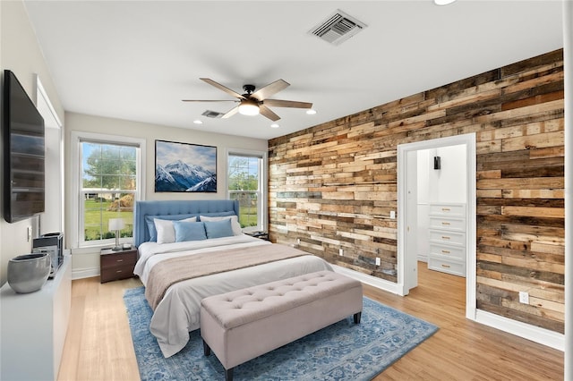 bedroom featuring light hardwood / wood-style floors, ceiling fan, and wooden walls