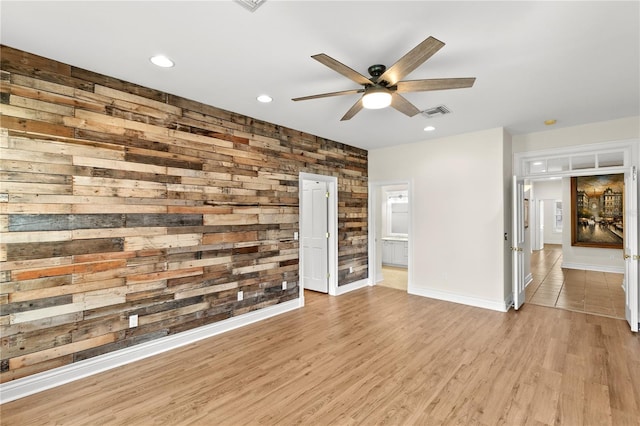 unfurnished living room with light hardwood / wood-style floors, ceiling fan, and wood walls