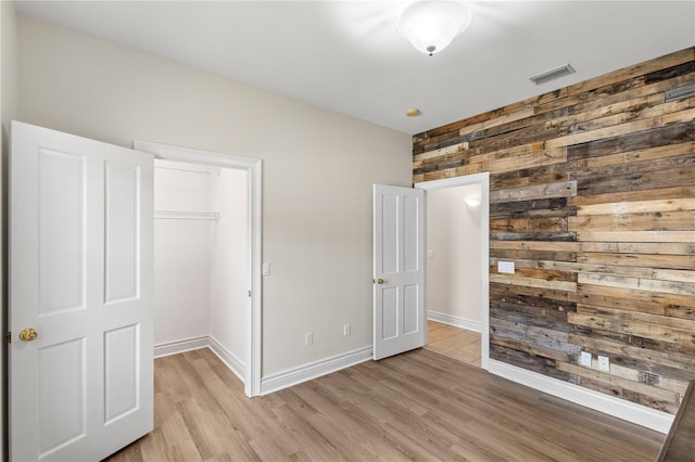 unfurnished bedroom featuring light hardwood / wood-style floors, a closet, and wooden walls