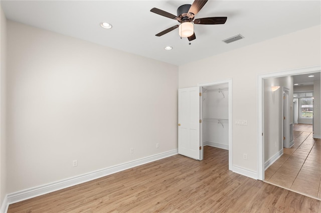 unfurnished bedroom with a closet, a walk in closet, ceiling fan, and light hardwood / wood-style flooring