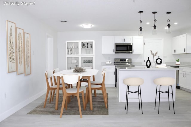 kitchen featuring appliances with stainless steel finishes, light wood-type flooring, pendant lighting, a center island, and white cabinetry