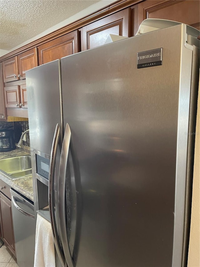 kitchen featuring stainless steel appliances, sink, light tile patterned floors, and a textured ceiling