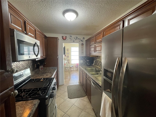 kitchen with appliances with stainless steel finishes, backsplash, a textured ceiling, sink, and light tile patterned floors