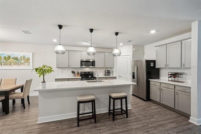 kitchen with decorative light fixtures, stainless steel appliances, dark hardwood / wood-style floors, and a kitchen island with sink