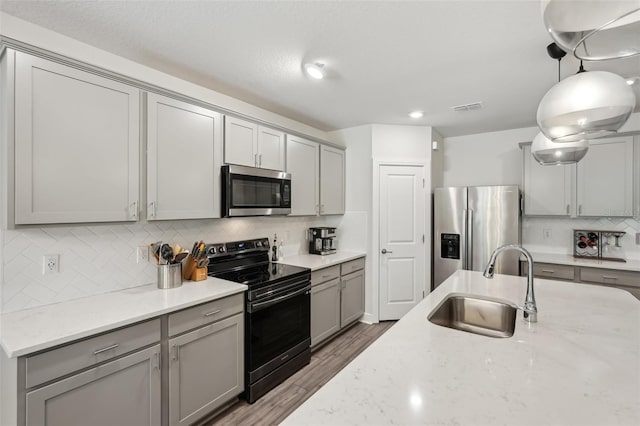 kitchen with sink, light stone counters, hardwood / wood-style floors, gray cabinets, and appliances with stainless steel finishes