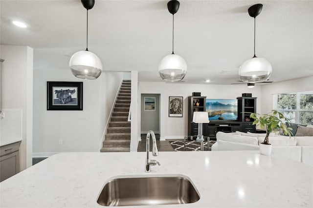 kitchen with light stone counters, sink, and hanging light fixtures