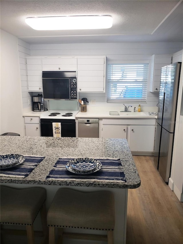 kitchen featuring a breakfast bar area, light hardwood / wood-style flooring, white cabinets, and appliances with stainless steel finishes