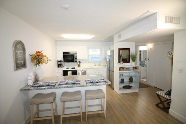 kitchen featuring kitchen peninsula, stainless steel appliances, white cabinets, light hardwood / wood-style floors, and a breakfast bar area