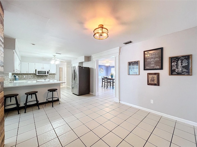 kitchen featuring kitchen peninsula, appliances with stainless steel finishes, tasteful backsplash, a kitchen bar, and white cabinetry