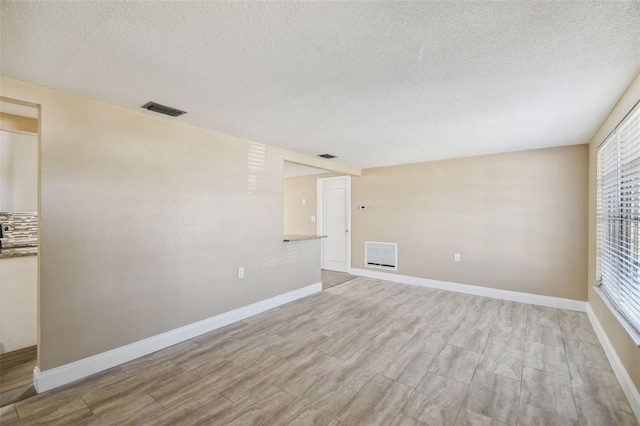 spare room featuring plenty of natural light, a textured ceiling, and light hardwood / wood-style flooring