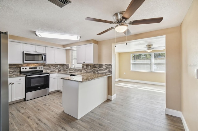 kitchen featuring kitchen peninsula, light wood-type flooring, dark stone counters, stainless steel appliances, and white cabinets