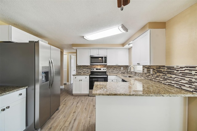 kitchen with sink, kitchen peninsula, light wood-type flooring, appliances with stainless steel finishes, and white cabinetry