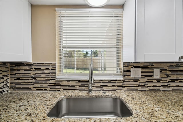 kitchen featuring light stone countertops, decorative backsplash, white cabinetry, and sink