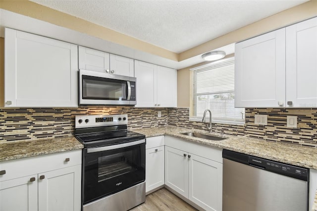 kitchen with light stone countertops, white cabinetry, sink, and appliances with stainless steel finishes