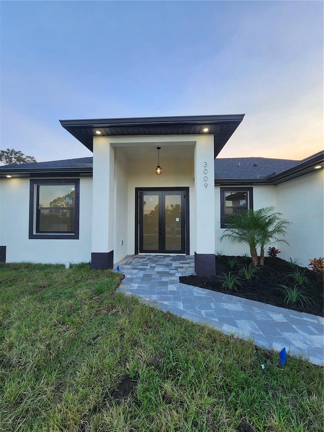 exterior entry at dusk featuring a lawn and french doors