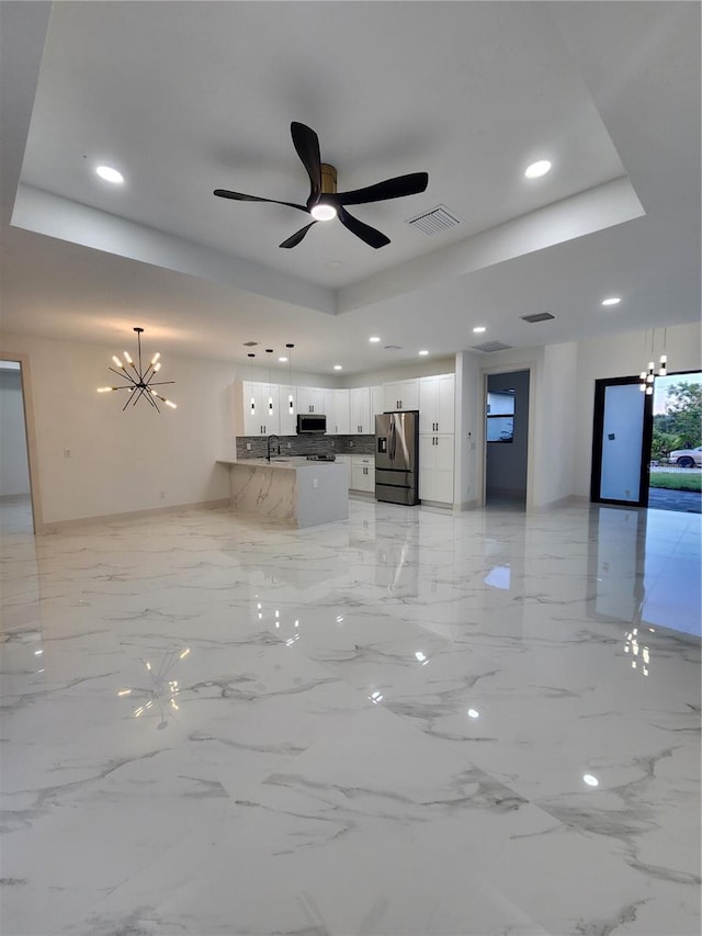 unfurnished living room featuring ceiling fan with notable chandelier, a raised ceiling, and sink