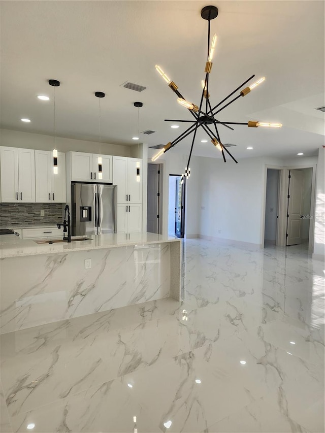 kitchen featuring sink, light stone counters, stainless steel refrigerator with ice dispenser, pendant lighting, and white cabinets