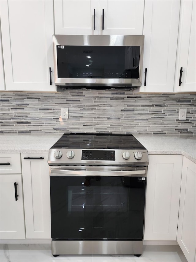 kitchen with backsplash, white cabinetry, light stone countertops, and appliances with stainless steel finishes