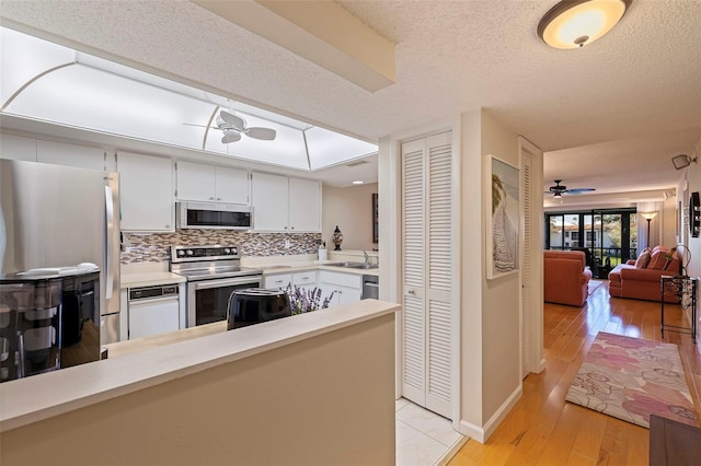 kitchen with ceiling fan, a textured ceiling, appliances with stainless steel finishes, light hardwood / wood-style floors, and kitchen peninsula