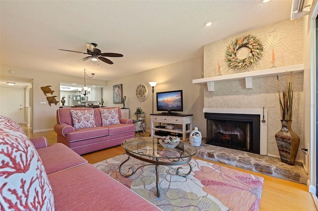 living room featuring a stone fireplace, ceiling fan with notable chandelier, a textured ceiling, and hardwood / wood-style flooring