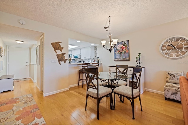 dining room featuring an inviting chandelier, light wood-style floors, baseboards, and a textured ceiling