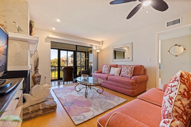 living room featuring a ceiling fan, wood finished floors, visible vents, and a textured ceiling