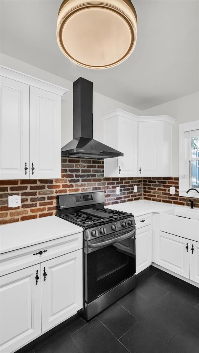 kitchen with white cabinets, gas range, sink, and wall chimney range hood