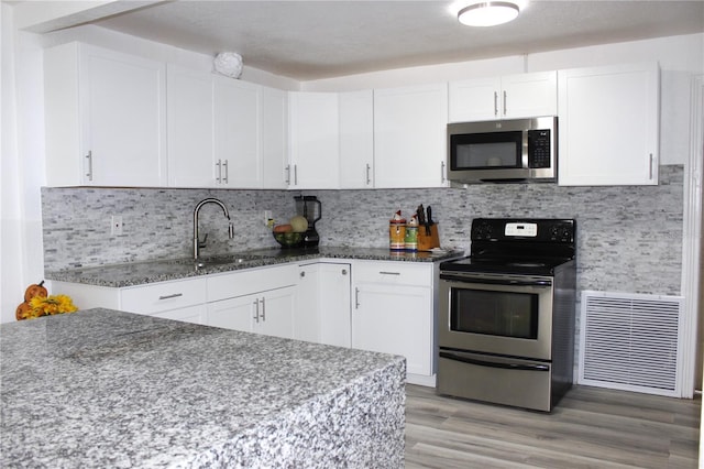 kitchen with wood-type flooring, stainless steel appliances, white cabinetry, and dark stone counters