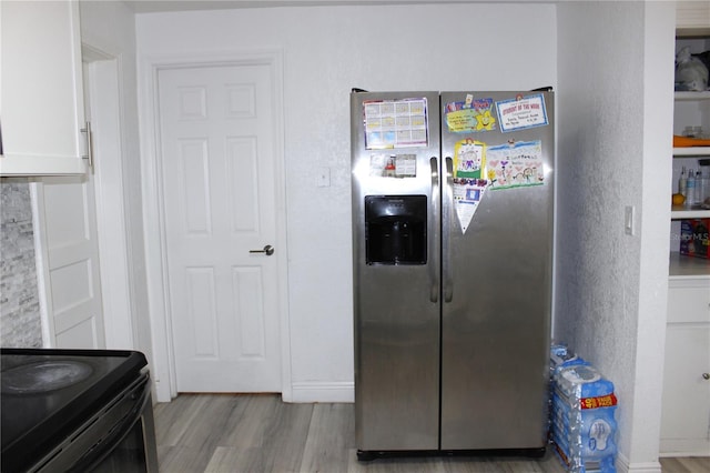 kitchen featuring black range with electric stovetop, stainless steel fridge with ice dispenser, light hardwood / wood-style flooring, and white cabinets