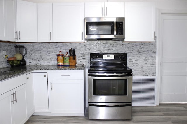 kitchen featuring hardwood / wood-style floors, stainless steel appliances, white cabinetry, and dark stone counters