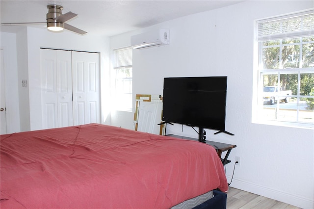 bedroom with ceiling fan, light hardwood / wood-style floors, a wall unit AC, and multiple windows