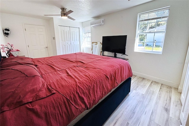 bedroom with ceiling fan, multiple windows, a wall unit AC, and light hardwood / wood-style flooring