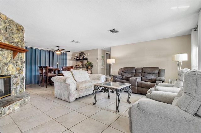 living room featuring ceiling fan, light tile patterned flooring, and a stone fireplace