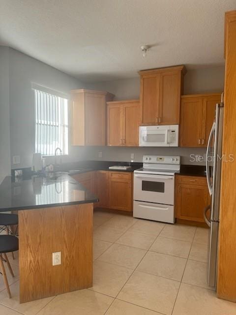 kitchen featuring kitchen peninsula, a kitchen breakfast bar, white appliances, sink, and light tile patterned floors