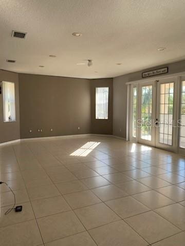 tiled spare room with french doors, a textured ceiling, and a wealth of natural light