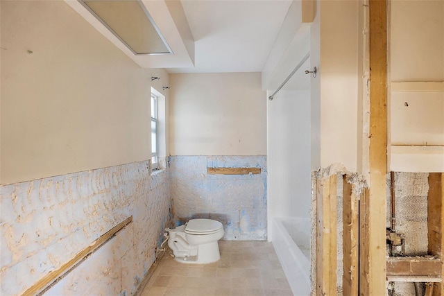 bathroom featuring a bathing tub, toilet, a wainscoted wall, tile walls, and walk in shower