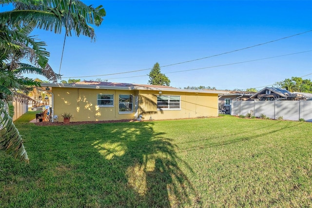 rear view of property featuring a yard, fence, and stucco siding