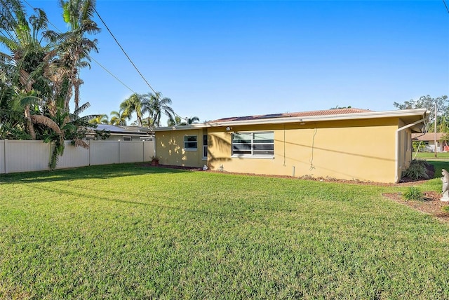 rear view of house featuring a yard, fence, and stucco siding