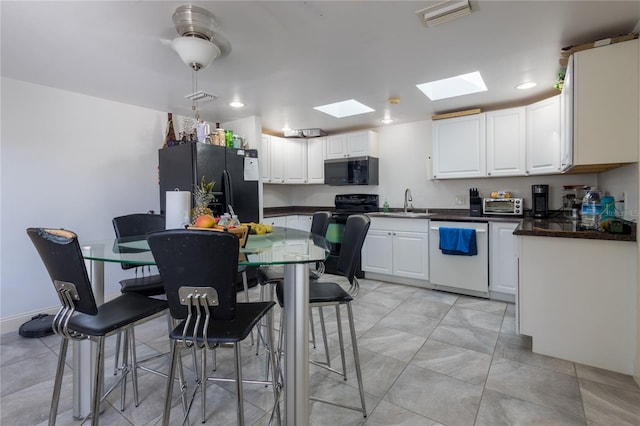 kitchen with black appliances, white cabinets, sink, and a skylight