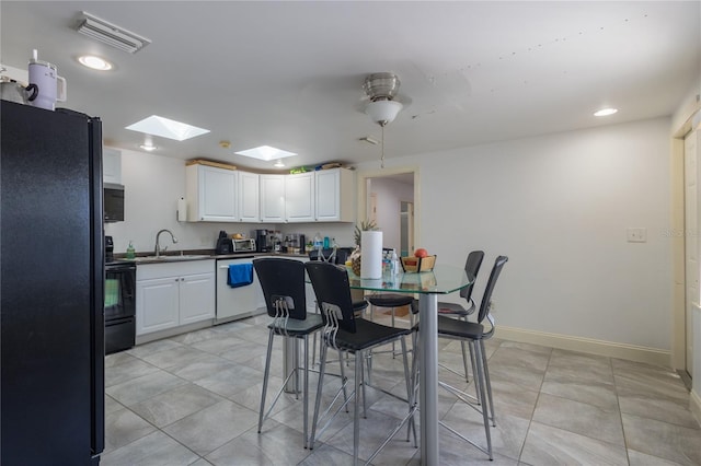 kitchen featuring a skylight, ceiling fan, sink, black appliances, and white cabinetry