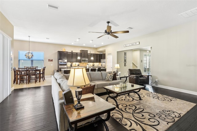 living room featuring dark wood-type flooring and ceiling fan with notable chandelier