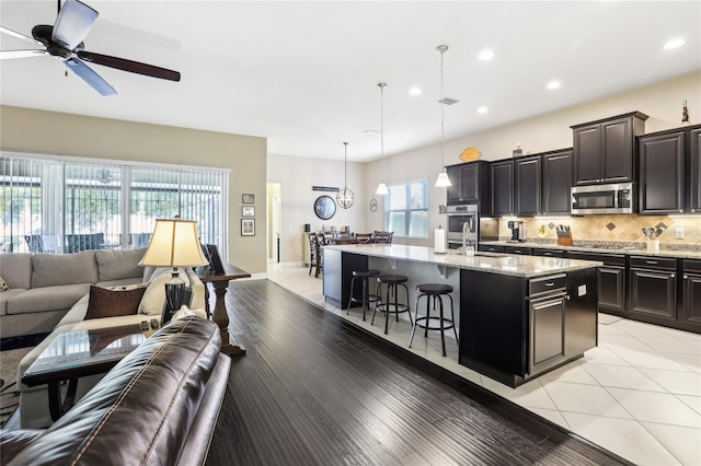 kitchen with an island with sink, stainless steel appliances, decorative backsplash, hanging light fixtures, and a breakfast bar