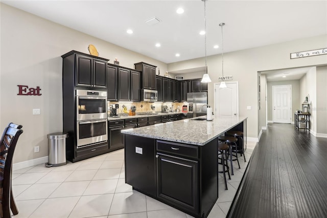 kitchen with pendant lighting, a kitchen bar, stainless steel appliances, tasteful backsplash, and a kitchen island with sink