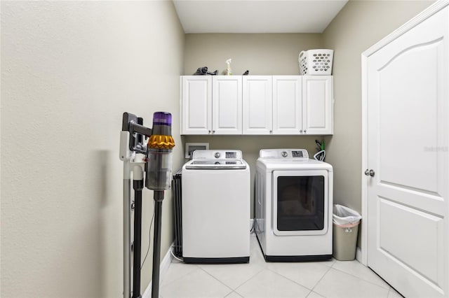 clothes washing area with cabinets, light tile patterned floors, and washing machine and clothes dryer